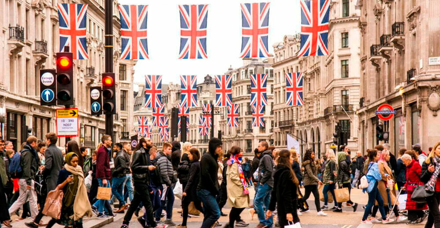 Rua movimentada de Londres, decorada com bandeiras britânicas e cheia de peões junto a uma estação de metro