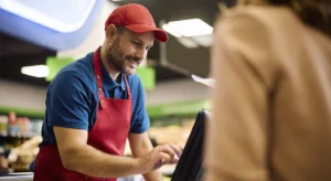 Um caixa masculino sorridente trabalhando na caixa registradora da loja.