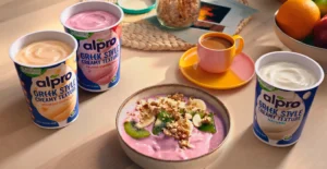 Três iogurtes Alpro, uma taça de iogurte com fruta e granola, chá e fruta numa mesa