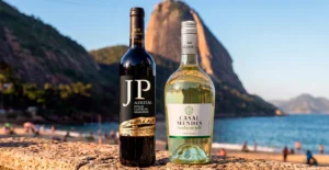 Duas garrafas de vinho, JP Azeitão e Casal Mendes Vinho Verde, junto a uma praia com o Pão de Açúcar ao fundo