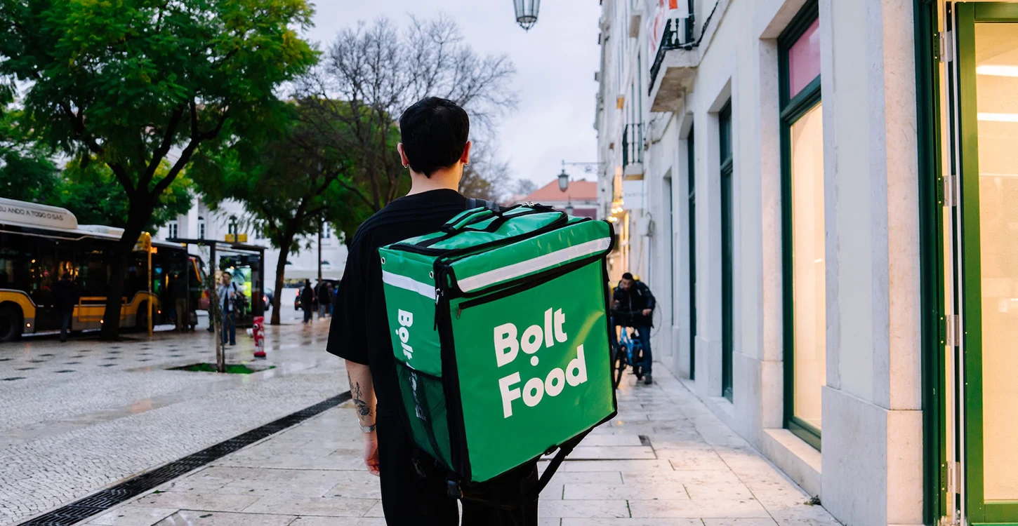 Entregador da Bolt Food caminha numa rua urbana com uma mochila térmica verde