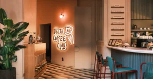 Interior de um café com balcão, equipamentos de café e letreiro luminoso «Delta Coffee Club»