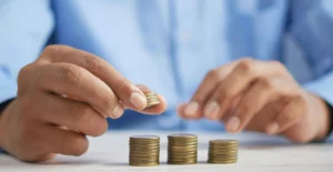Pessoa a contar moedas, com três pilhas de moedas sobre a mesa