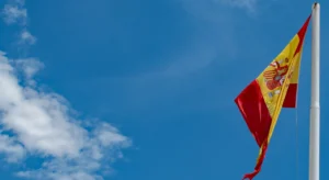 Bandeira de Espanha hasteada ao vento contra um céu azul com nuvens