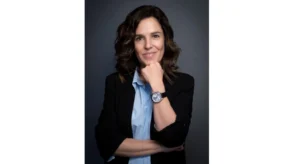 Retrato de uma mulher sorridente, com blazer preto e camisa azul, apoiada sobre a mão