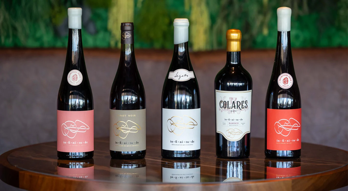 Cinco garrafas de vinho tinto, incluindo uma de Colares, alinhadas sobre uma mesa de madeira