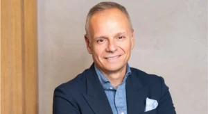Homem sorridente de cabelo grisalho, com blazer azul-escuro e camisa azul-clara