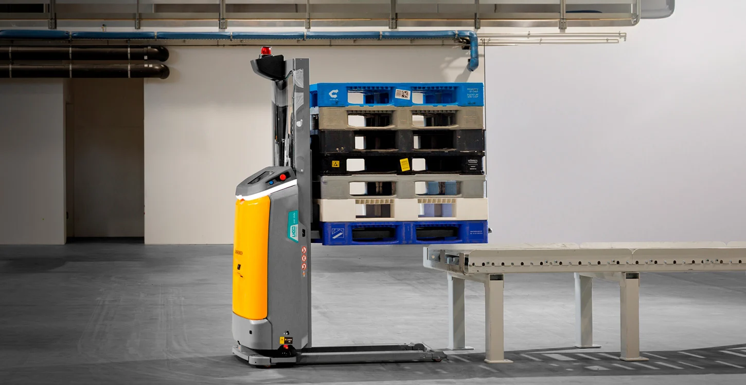 Empilhador elétrico junto a uma pilha de paletes e a um transportador industrial