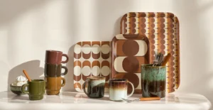 Composição de canecas, chávenas, jarro e tabuleiros com padrões geométricos em tons castanhos e creme