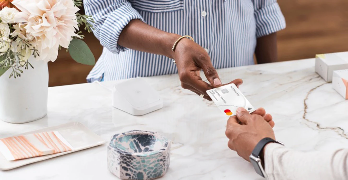 Uma pessoa entrega um cartão bancário Mastercard a outra sobre uma mesa