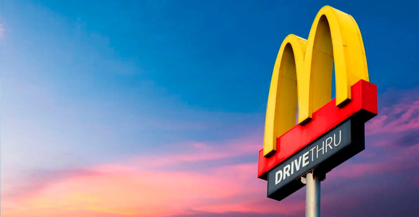 Letreiro do McDonald’s com a indicação «DRIVE THRU», contra um céu ao entardecer