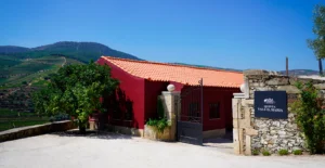 Entrada da Quinta Vale D. Maria, com edifício vermelho e vinhas em socalcos ao fundo