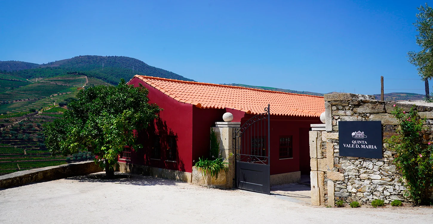 Entrada da Quinta Vale D. Maria, com edifício vermelho e vinhas em socalcos ao fundo