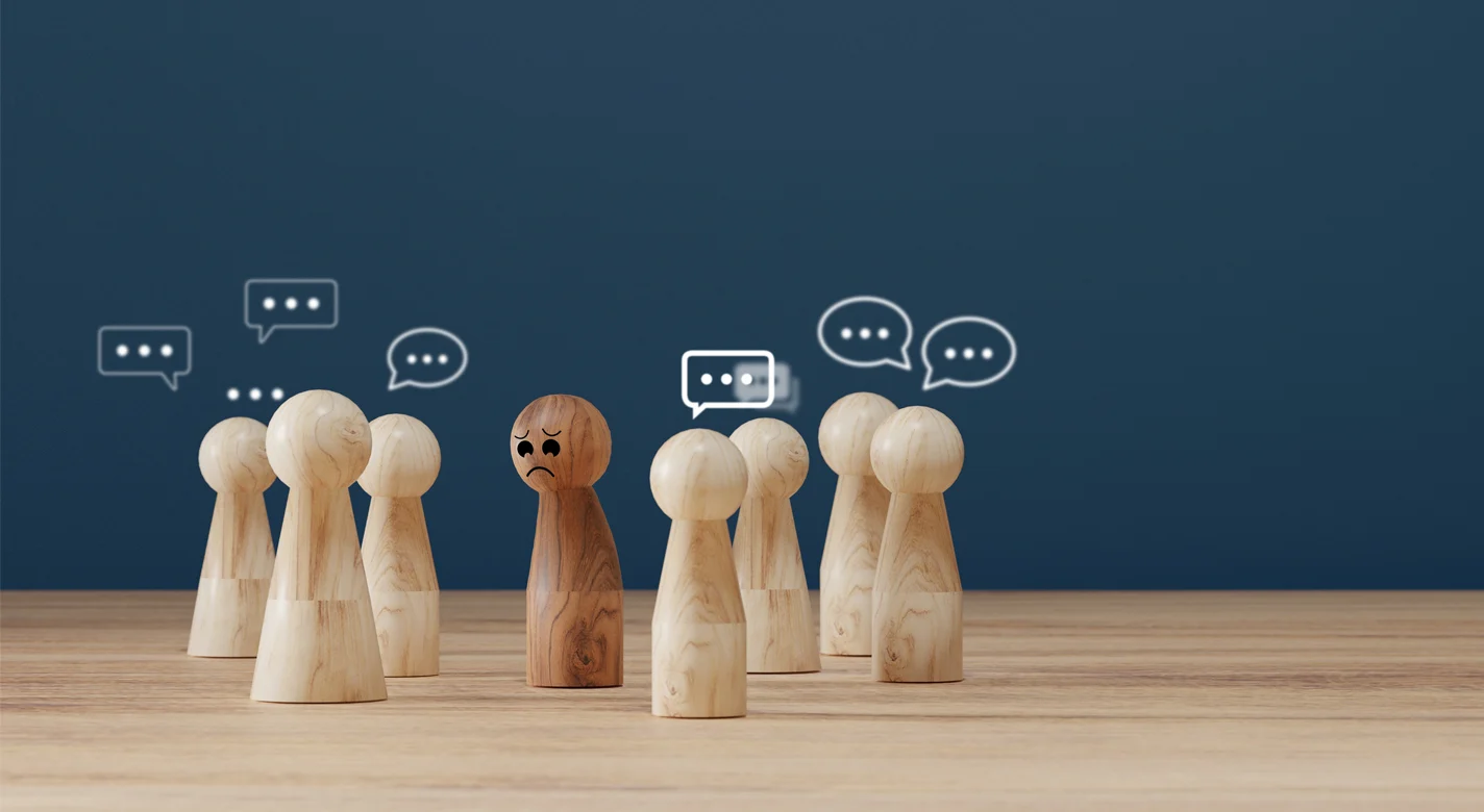 Figuras de madeira conversam em grupos, enquanto uma figura castanha permanece isolada e triste