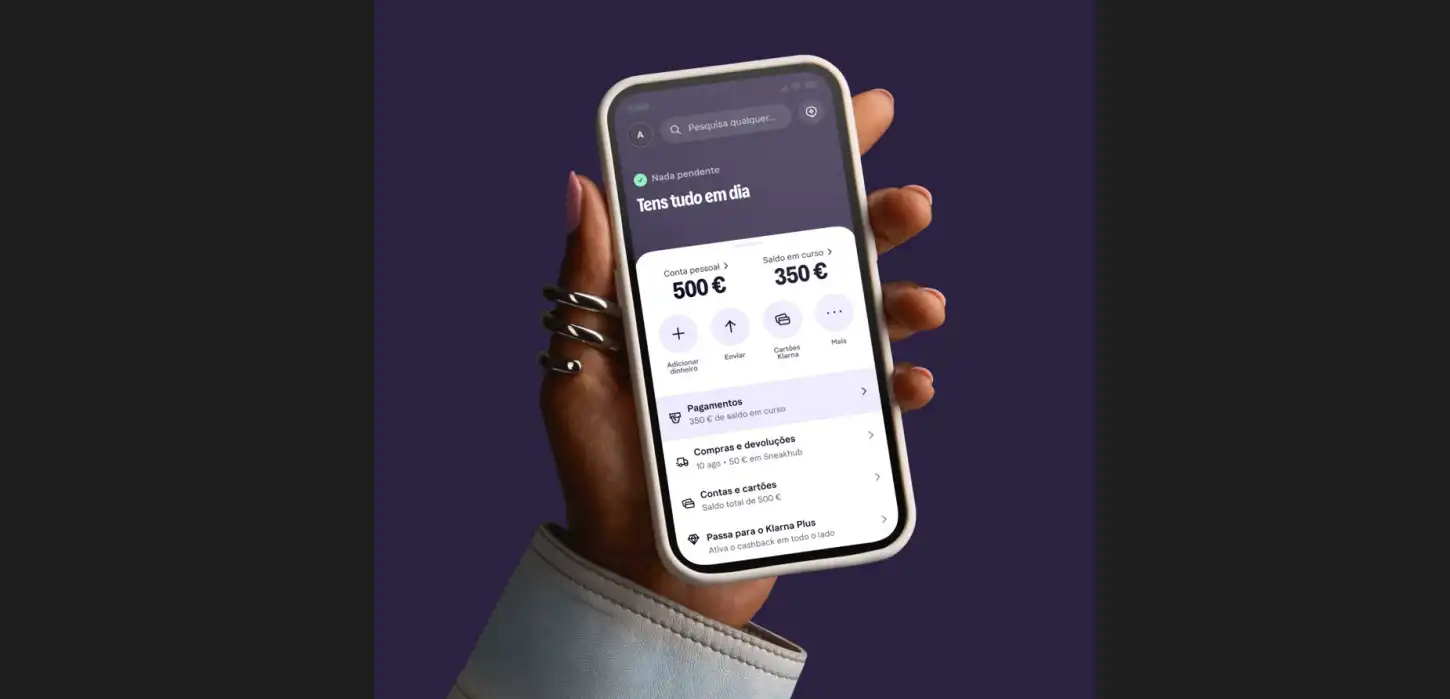 Mão segura um telemóvel com uma aplicação financeira que mostra 500 € na conta e 350 € de saldo disponível