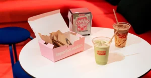 Mesa com uma caixa de cookies, dois copos de bebidas e um dispensador de açúcar Vigor