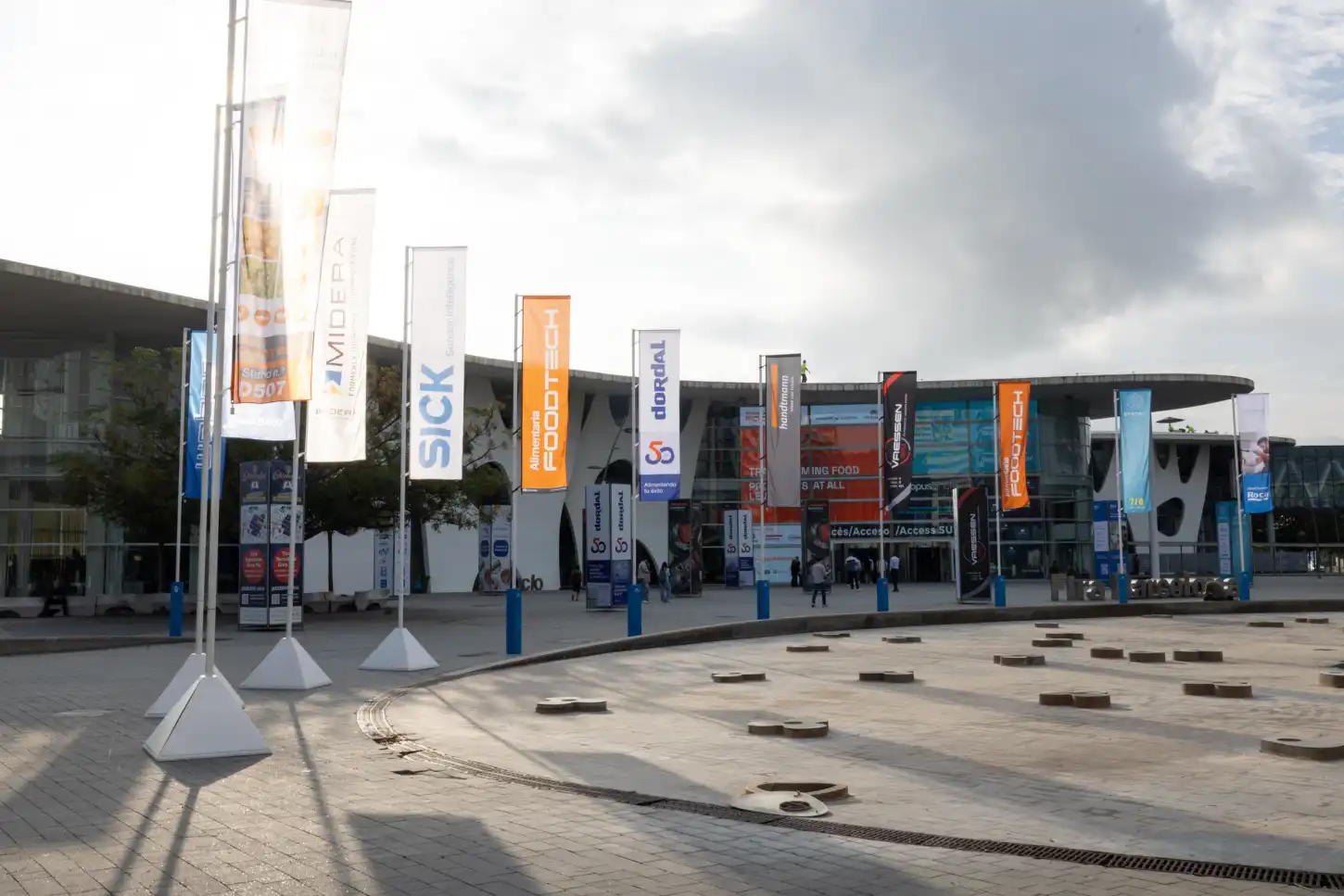 Entrada de um centro de exposições com bandeiras de patrocinadores e visitantes