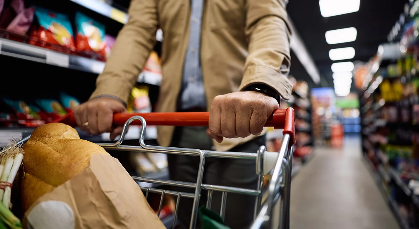 Pessoa a empurrar um carrinho de compras com pão num corredor de supermercado