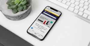 Smartphone a navegar no site da refurbed, pousado numa secretária junto a um teclado e uma suculenta